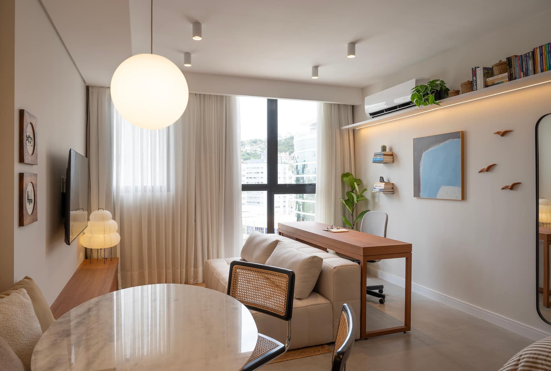 Sala iluminada com janela ampla, sofá e mesa de trabalho